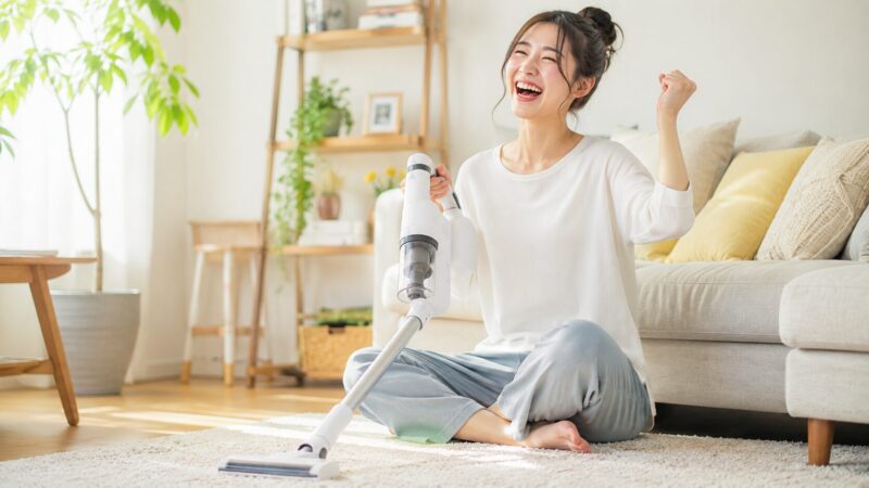 IC-FAC3を使って掃除を終えた女性が満面の笑顔を見せる、明るく清潔感のあるリビングと一般的なデザインのコードレス掃除機のイメージ写真