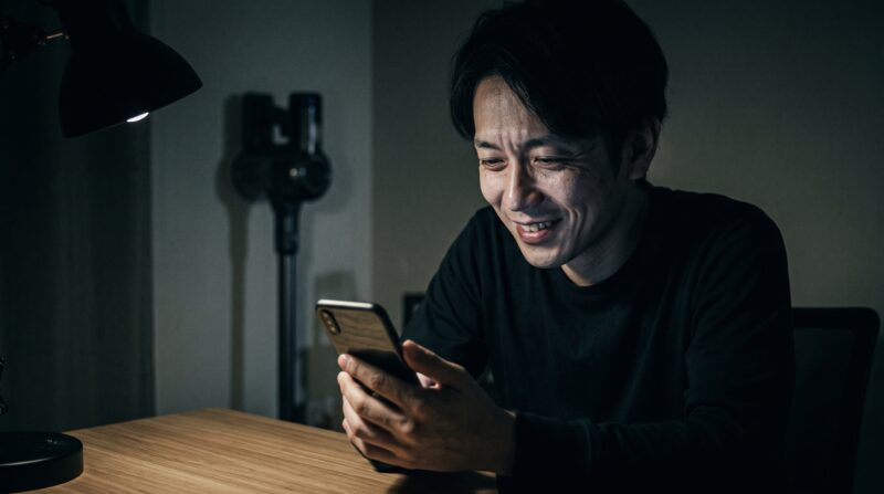 コードレス掃除機SCD-124PDの口コミをスマートフォンで見て笑顔で満足する日本人男性