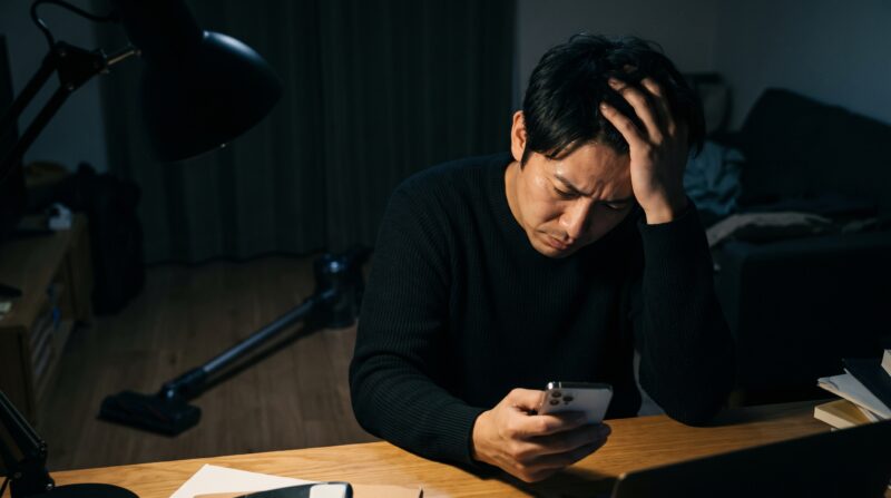 深夜にスマートフォンで掃除機の口コミを調査し、頭を抱えて深く悩む日本人男性