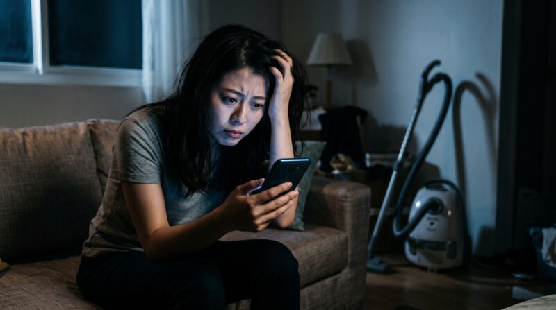 掃除機の口コミや評判をスマホで調べて不安に悩んでいる女性の様子。