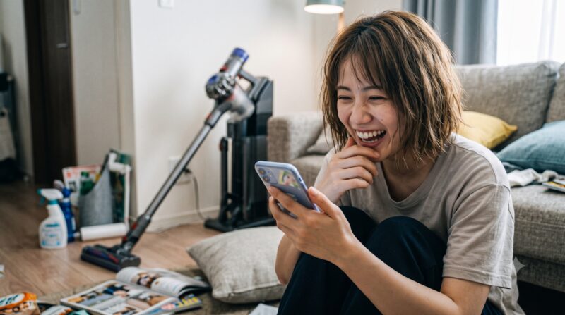 掃除機のある明るいリビングで、スマートフォンに表示された星5つの高評価レビューを見て笑顔で喜ぶ女性。